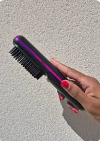 Cliente tenant une brosse chauffante lissante noire et rose en main, photo réelle du produit utilisé à domicile, vue du design et des picots chauffants.