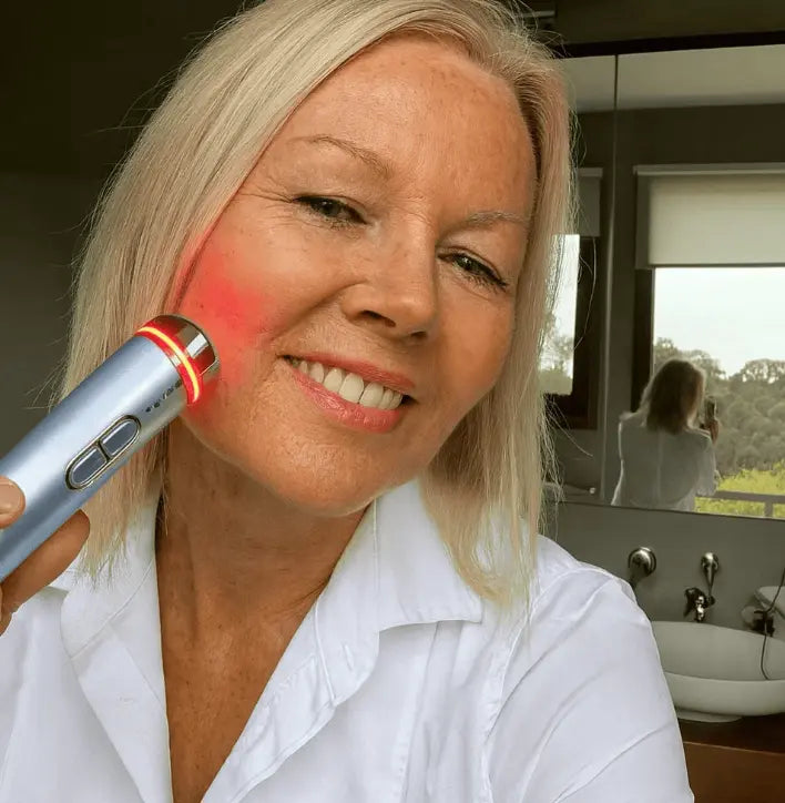 "Portrait d'une cliente souriante utilisant la fonction lumière rouge de l'appareil HIFU Lift Pro sur sa joue."